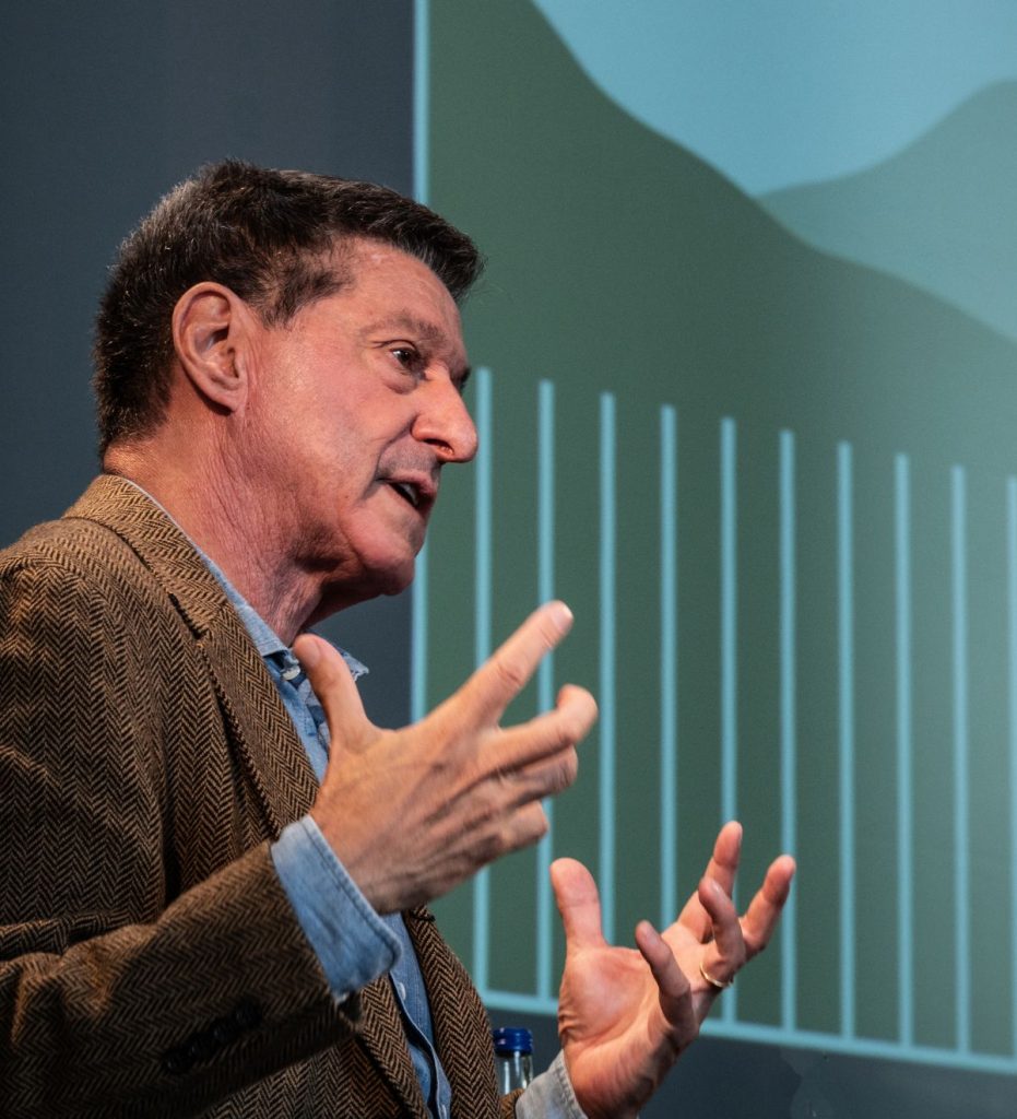 A close-up of speaker Jon Sopel at the Braemar Literary Festival with his hands up as he speaks to an audience.