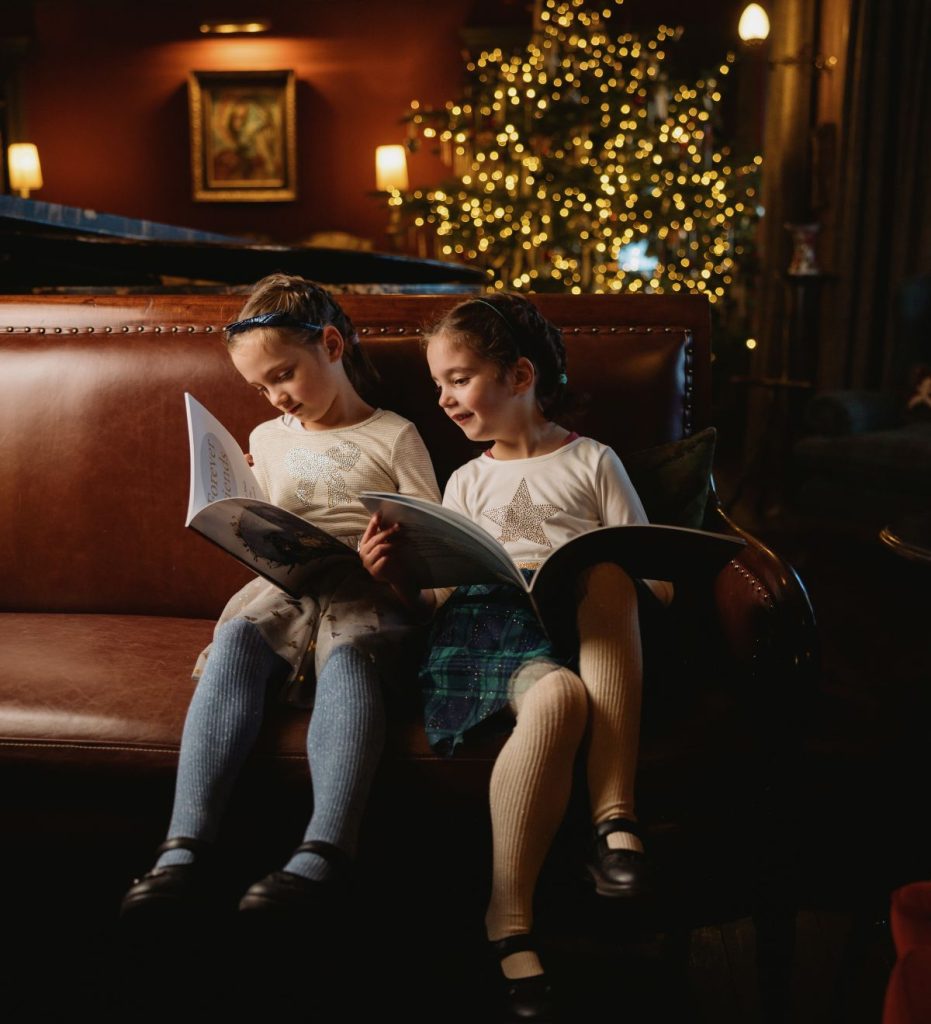 Two girls sitting on a sofa in front of a Christmas reading stories on Christmas Eve