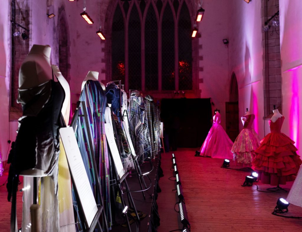 Mannequins with fashionable dresses on displayed in a church lit with pink uplights.