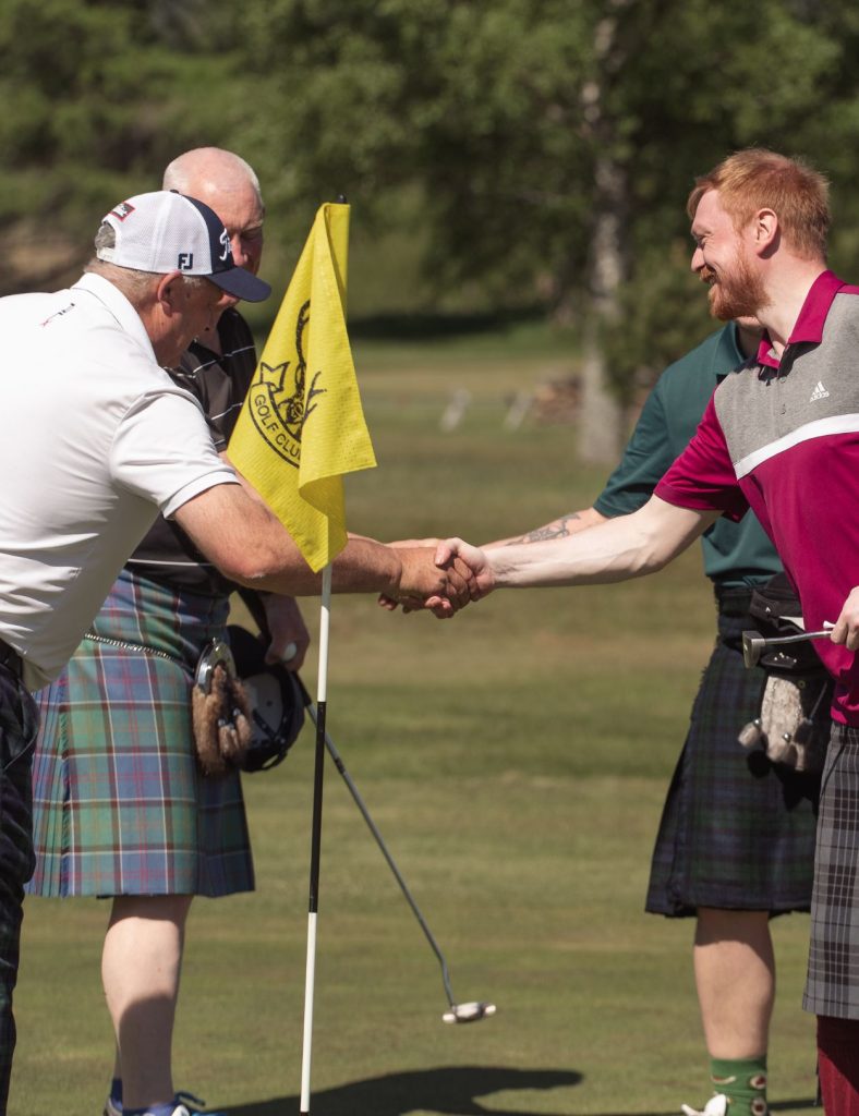 Two male golfers shaking hands on a golf green in front of a hole.